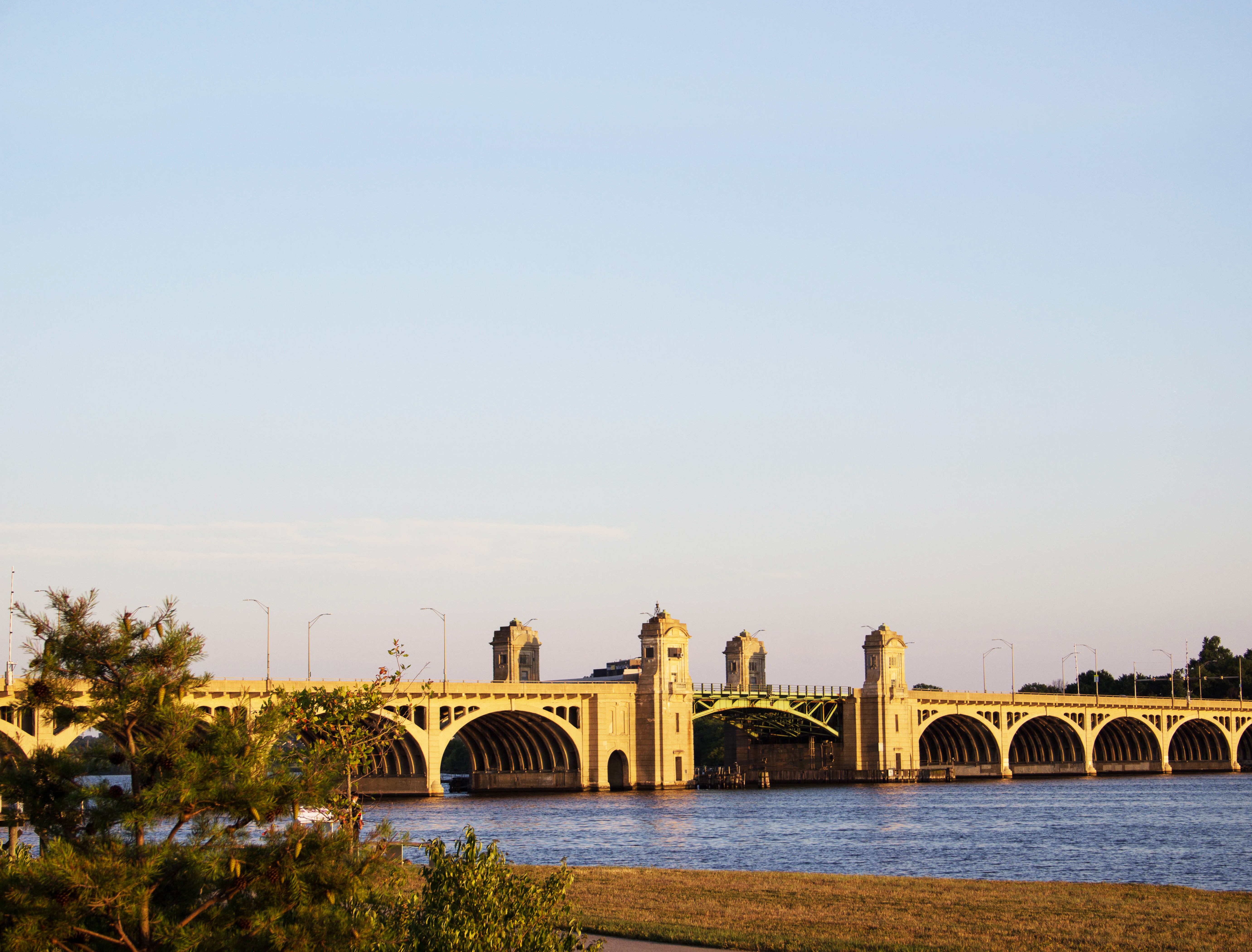 View of the Hanover Street/Vietnam Veterans Memorial Bridge. There are no clouds in the sky and the sun is setting with warm light on the bridge and water.