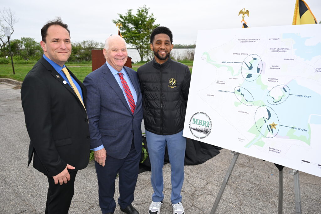 South Baltimore Executive Director Brad Rogers, Senator Ben Cardin, Mayor Brandon Scott are smiling and standing next to a large map outlining MBRI wetland restoration projects.