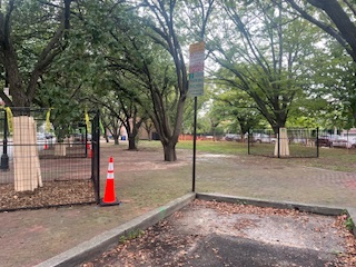 View of the corner of the park and trees which are partially sectioned off by construction fencing.