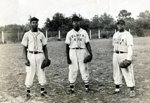 Black and white photo. Three Baltimore Black Sox baseball players are standing in a field in their uniforms looks at the camera.