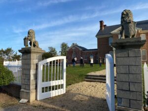 View of the front entrance of the Museum, which has a gravel path going up to two cement lions with white gates.