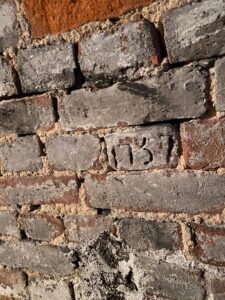 Brick wall with one brick has "1757" carved into it.